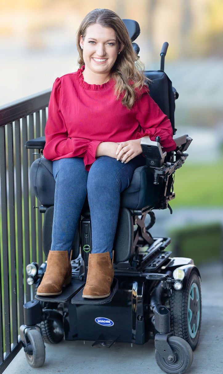 Woman in a red sweater and blue jeans sitting in a power wheelchair on a balcony.